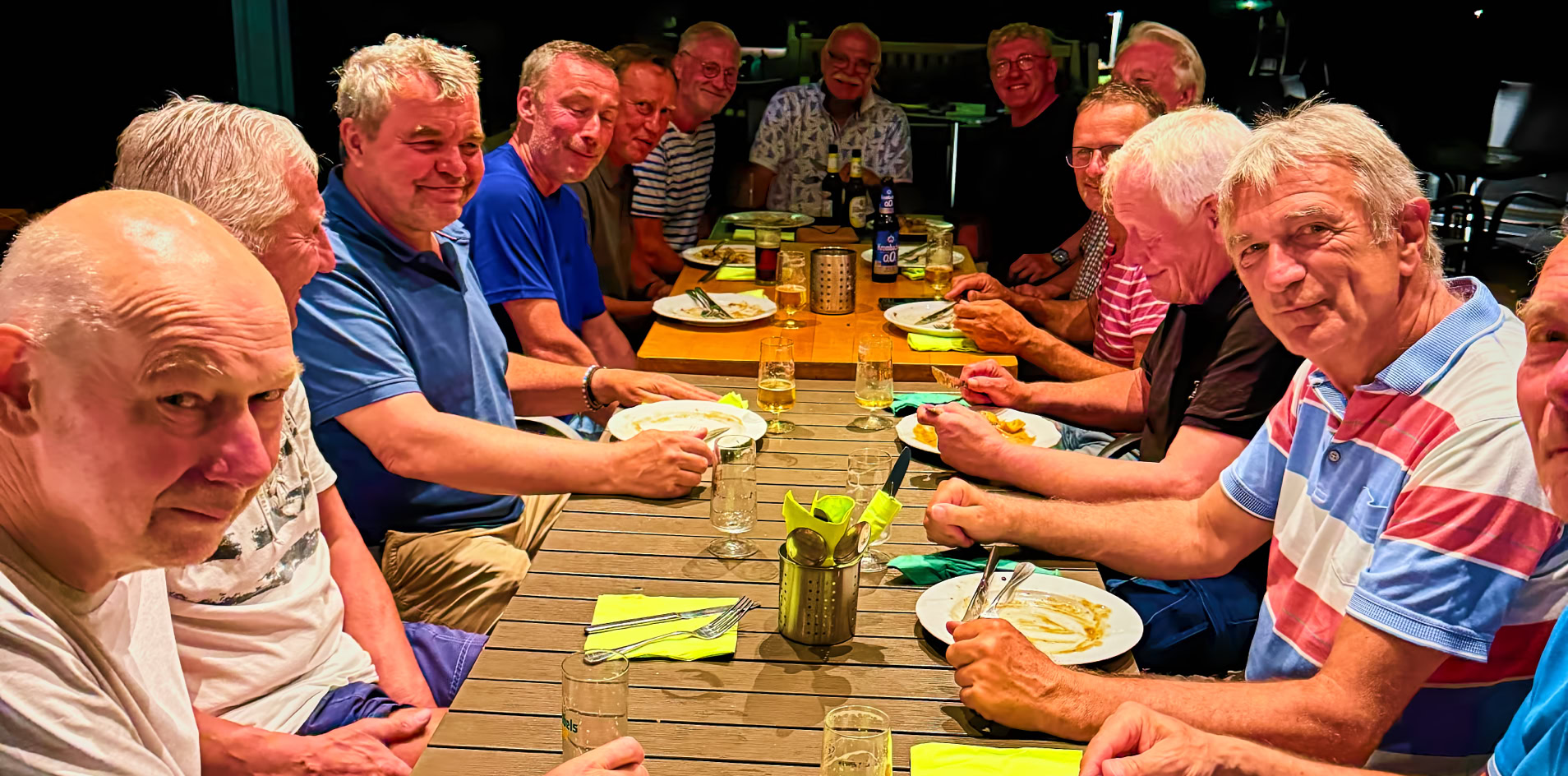 Eine Gruppe &auml;lterer M&auml;nner sitzt an einem langen Holztisch im Freien und isst gemeinsam.