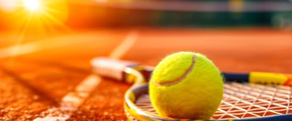 Tennisball auf einem Tennisschl&auml;ger auf einem Sandplatz bei Sonnenuntergang.