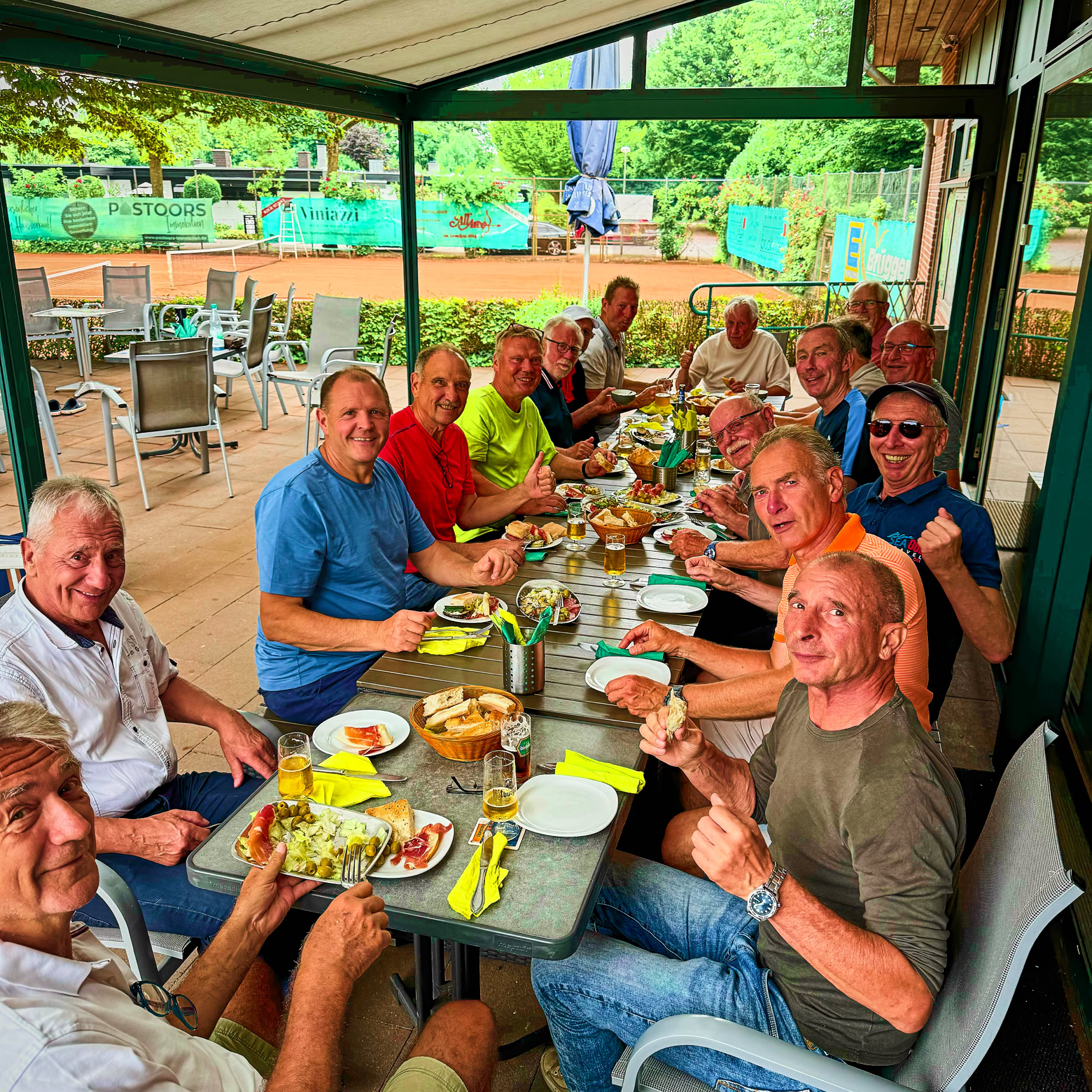 Eine Gruppe von Menschen sitzt an einem langen Tisch im Freien und isst gemeinsam.