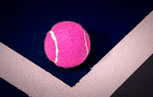 Ein pinker Tennisball liegt auf einem dunkelblauen Tennisplatz mit wei&szlig;en Linien.