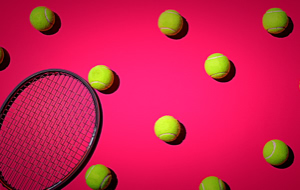Tennisschl&auml;ger und mehrere gelbe Tennisb&auml;lle auf einem pinken Hintergrund.