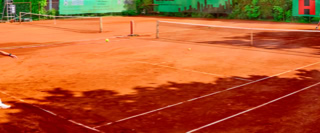 Zwei Personen spielen Tennis auf einem Sandplatz, umgeben von gr&uuml;nen W&auml;nden und B&auml;umen.