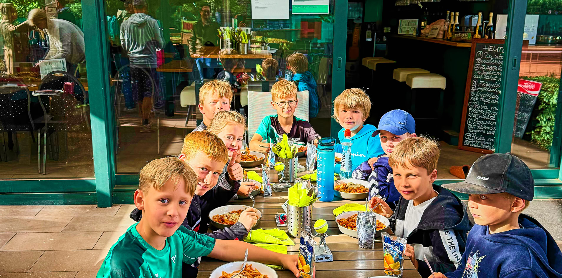 Kinder sitzen an einem Tisch im Freien und essen gemeinsam.
