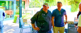 Mehrere Personen stehen und unterhalten sich in einem Au&szlig;enbereich mit St&uuml;hlen und Tischen.