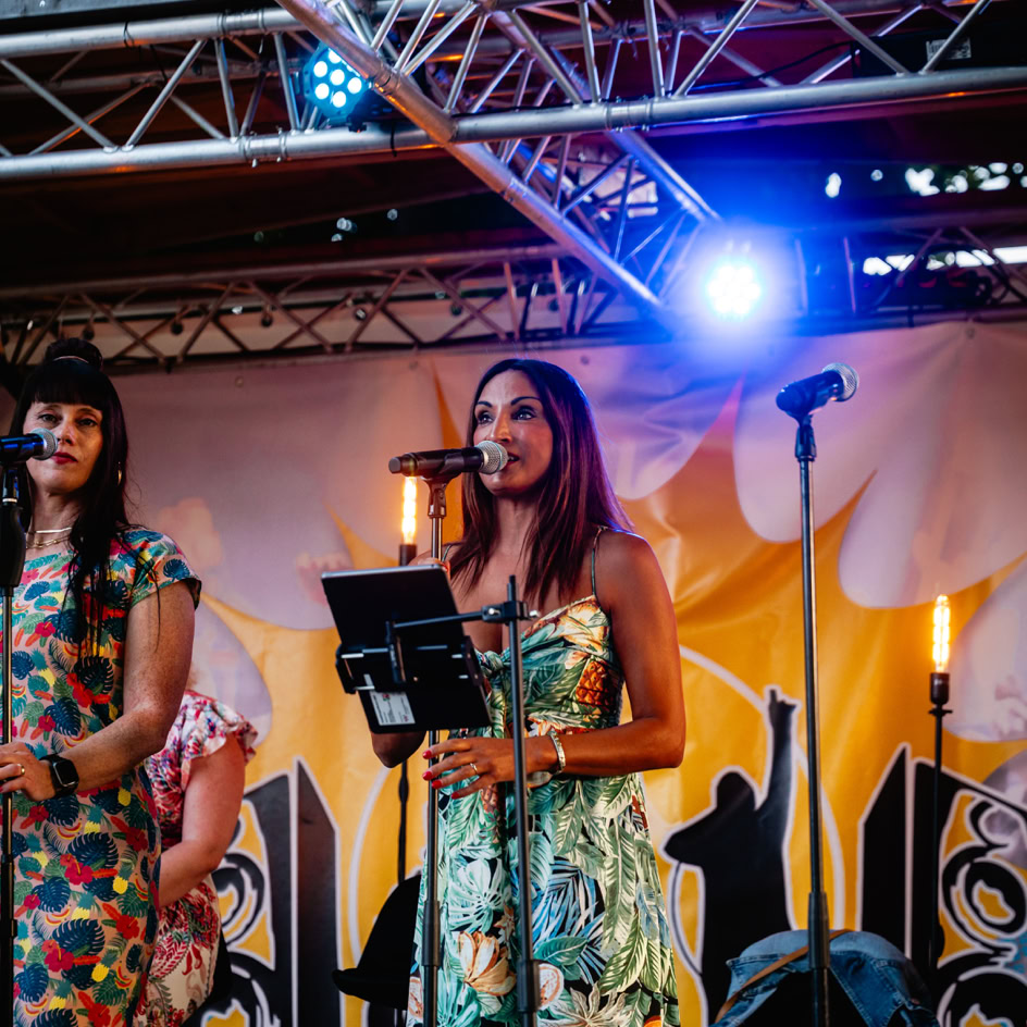 Zwei Personen stehen auf einer B&uuml;hne mit Mikrofonen, umgeben von bunten Lichtern und einem dekorativen Hintergrund.