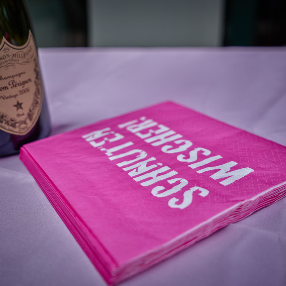 Eine Flasche Champagner und ein Stapel pinker Servietten mit der Aufschrift "SCHNITZER WISCHER" auf einem Tisch.