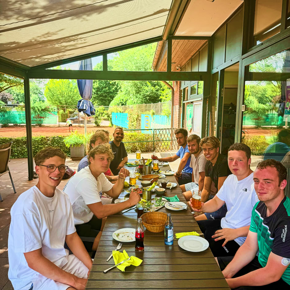 Eine Gruppe von Menschen sitzt an einem langen Tisch im Freien und isst gemeinsam.