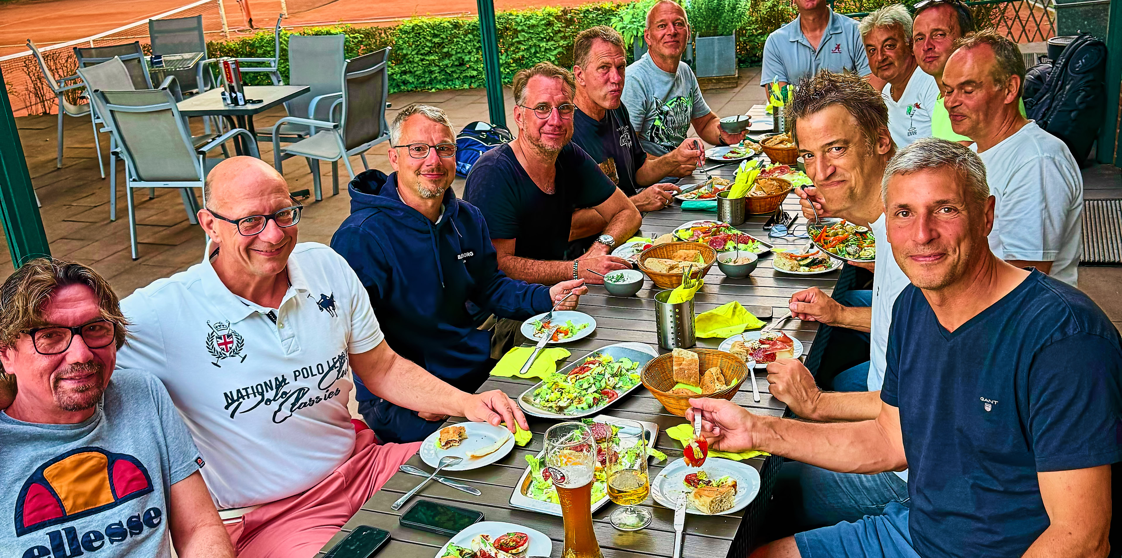 Eine Gruppe von Menschen sitzt an einem Tisch im Freien und isst gemeinsam.