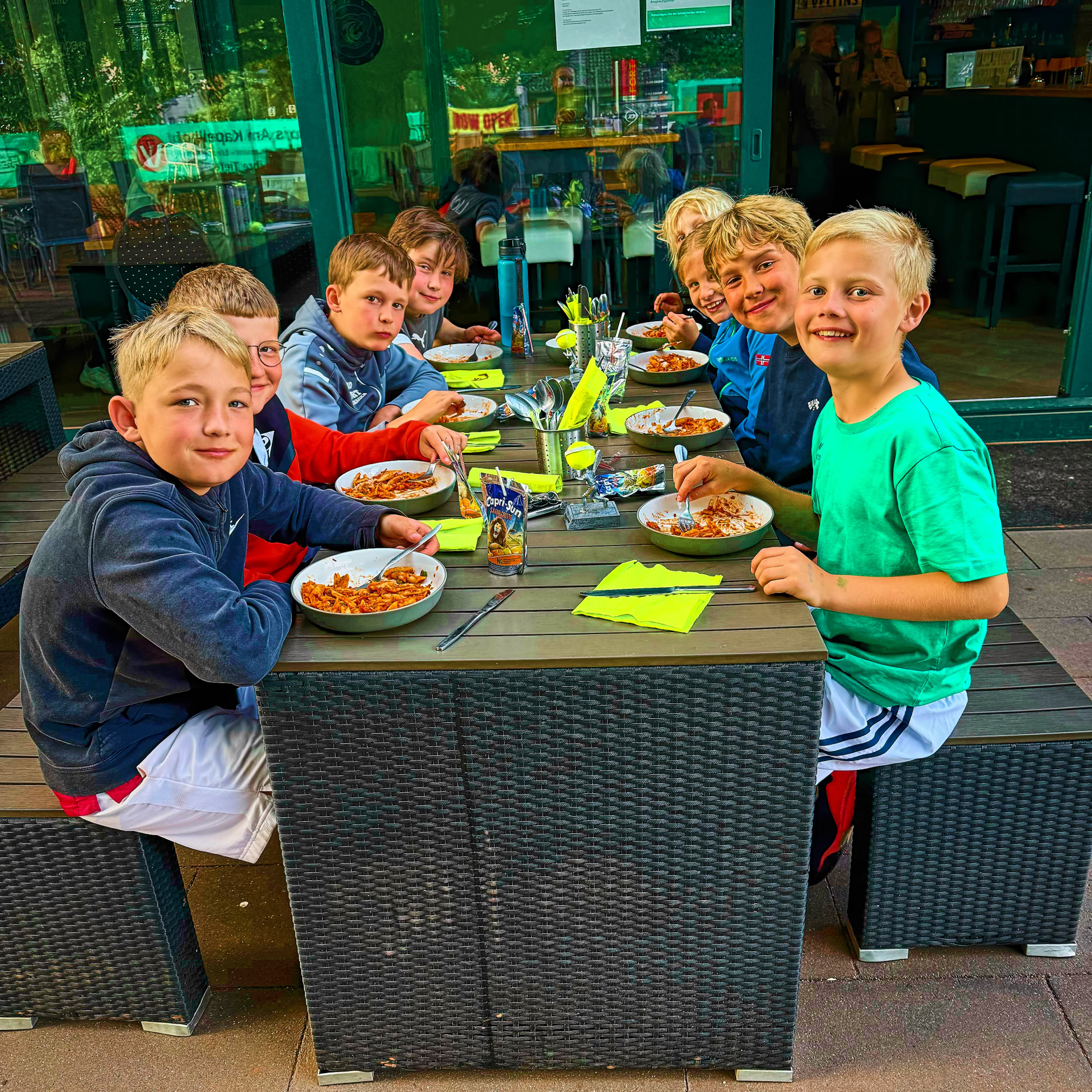 Sechs Kinder sitzen an einem Tisch im Freien und essen.