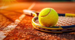Tennisball auf einem Tennisschl&auml;ger auf einem Sandplatz bei Sonnenuntergang.
