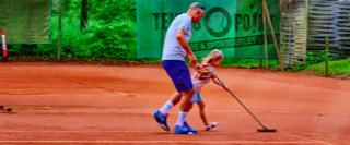Ein Erwachsener und ein Kind harken gemeinsam einen Sand-Tennisplatz.